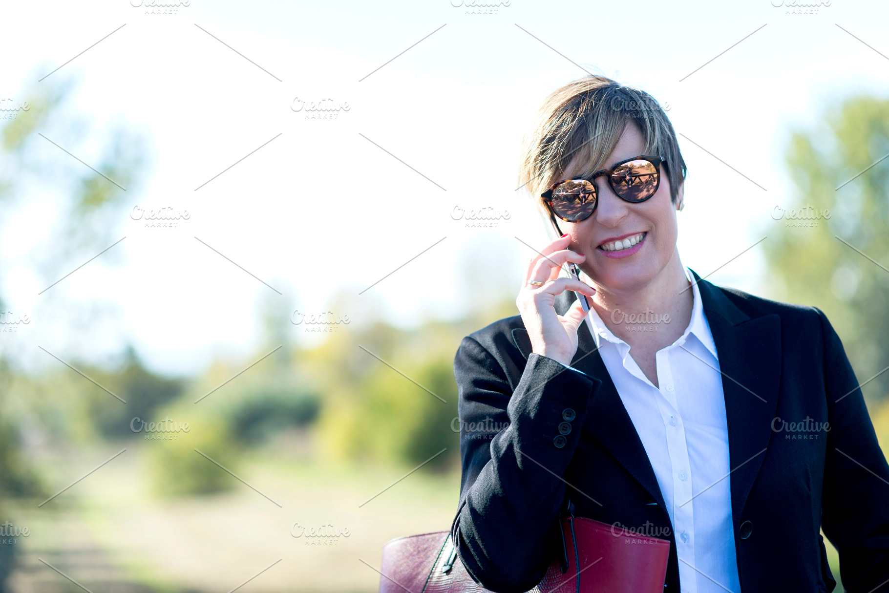 Smiling businesswoman talking on smartphone outdoors, a Photo by RF Images