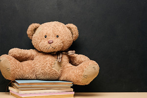 Brown teddy bear sitting on a stack of colorful books symbolizin, a School & Education Photo by ndanko