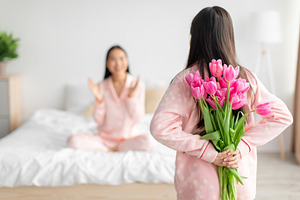 Teen girl hold bouquet of tulips behind back and congratulates asian millennial, a Photo by Prostock-Studio
