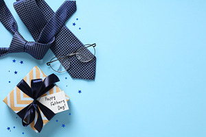 Flat lay composition with Fathers Day gift, necktie, eyeglasses, confetti on pa