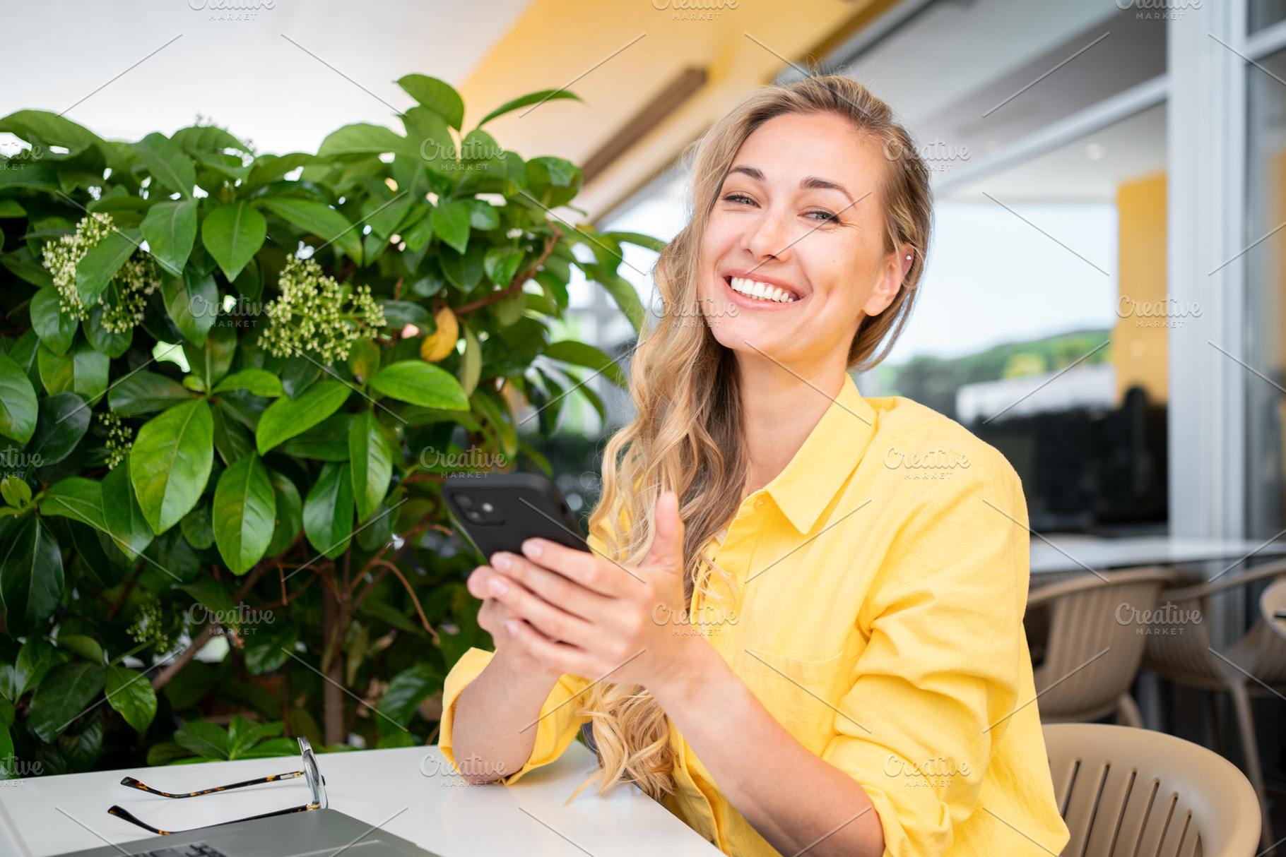 Happy freelancer woman holding smartphone at restaurant table, a Person Photo by andreonegin market