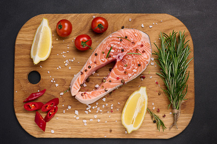 Raw salmon steak on a wooden cutting board, lemon slices, spices, a Food & Drink Photo by ndanko