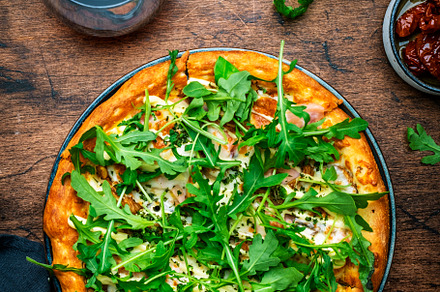 Hot pizza with mozzarella cheese, ham, pesto sauce and fresh aru