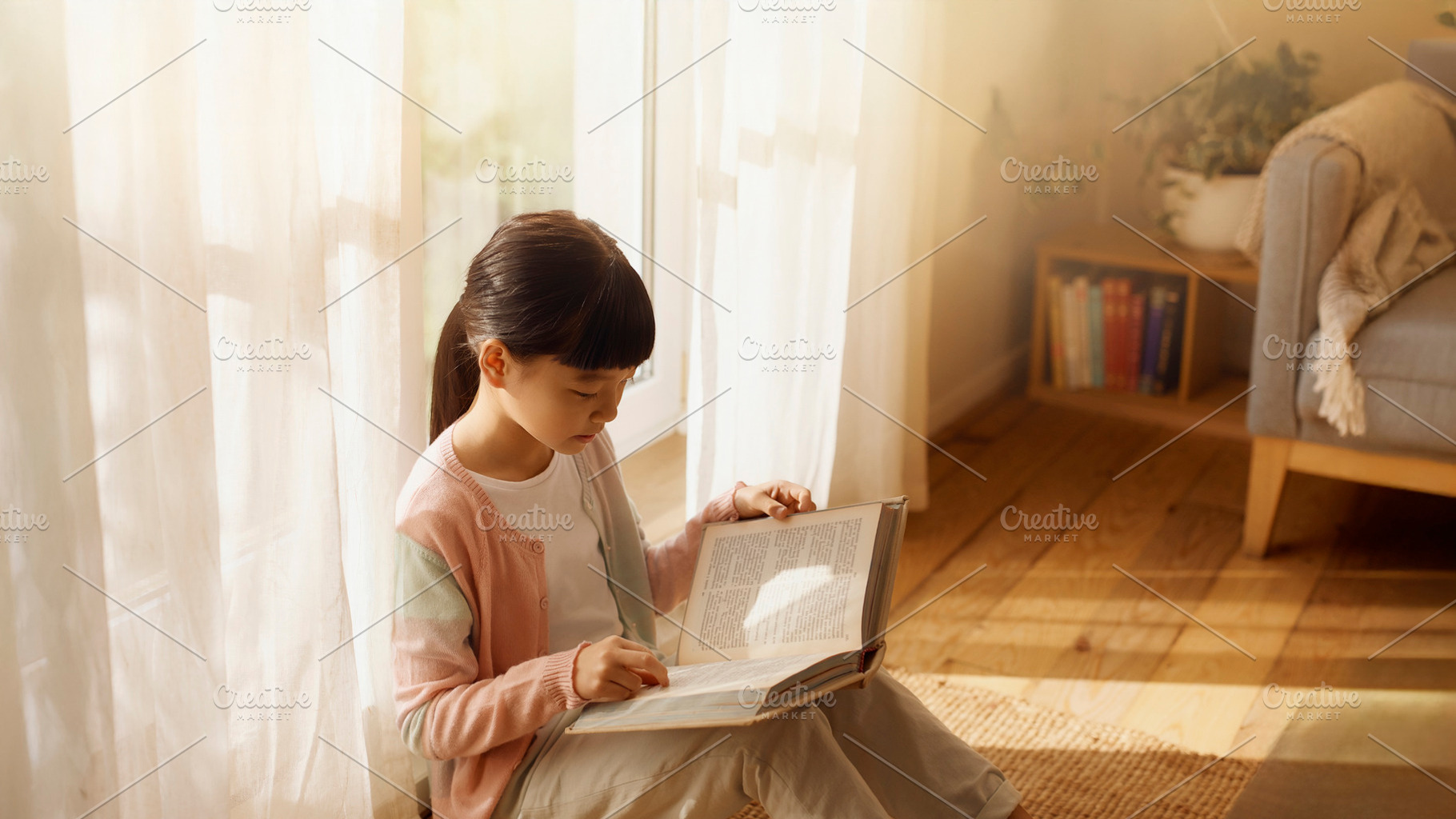 Asian girl sitting on the floor near a bright window, holding an, a School & Education Photo by DanFLCreativo