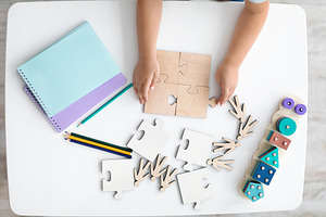 Top view of child holding wooden puzzle pieces, little hands connecting jigsaw, a Photo by Prostock-Studio