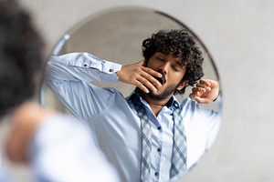 Sleepy indian businessman yawning while standing in bathroom and looking at his, a Person Photo by Prostock-Studio
