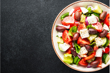 Greek salad in craft plate on black