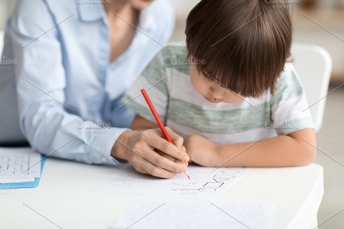 Early development training. Concentrated little boy pupil painting with teacher, a Photo by Prostock-Studio (Photo 1 of 2)