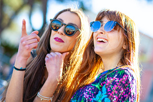 Two young women wearing sunglasses pointing and laughing outdoors, a Person Photo by Antonio Gravante Market