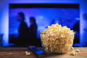 A glass bowl of popcorn and remote control in the background the TV works. Even, a Food & Drink Photo by Budarinphoto