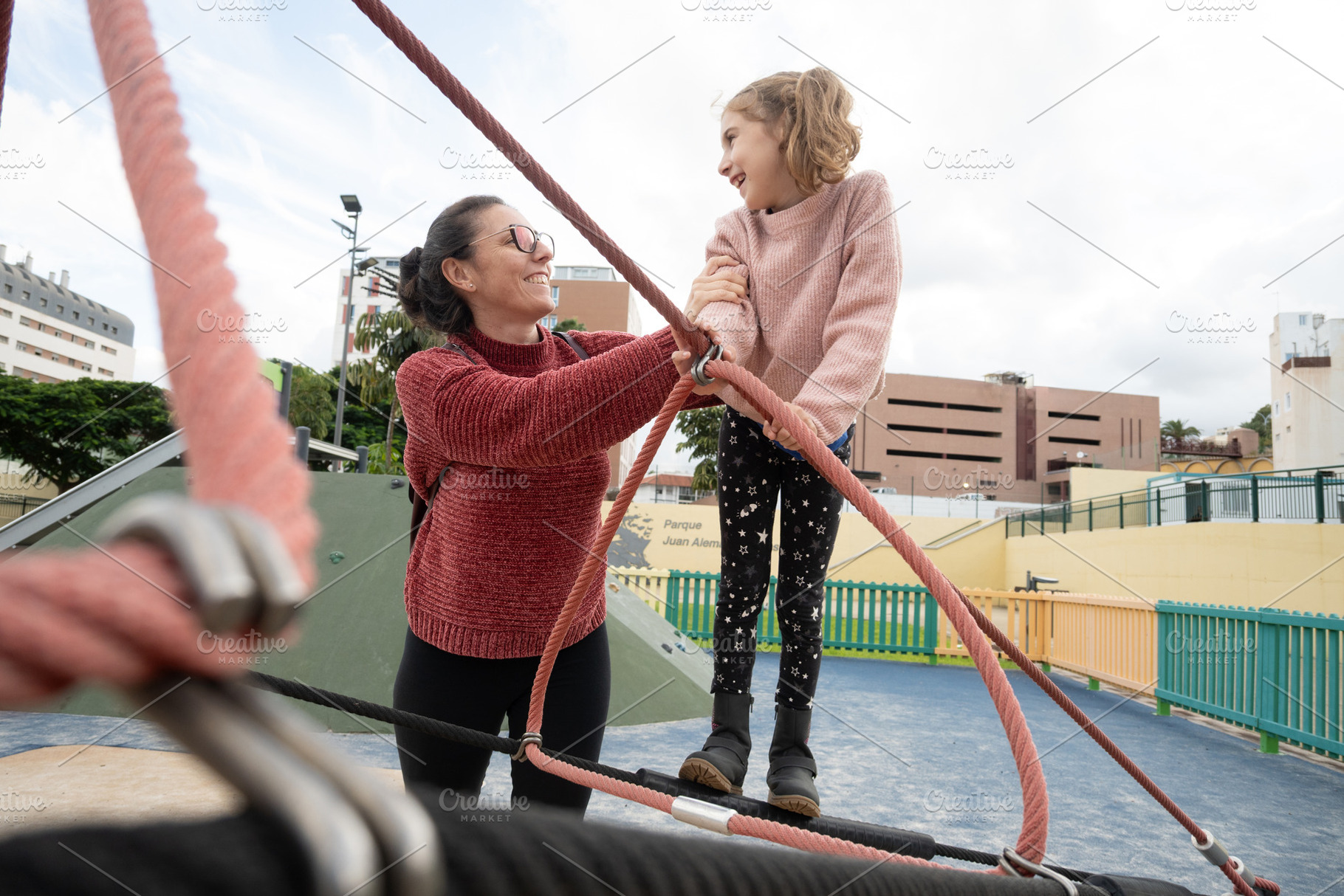 Mother helping her daughter balance on playground climbing ropes, a Person Photo by etorres69
