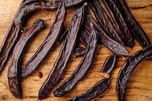 a group of ripe carob pods on a wooden table, a Photo by Nito
