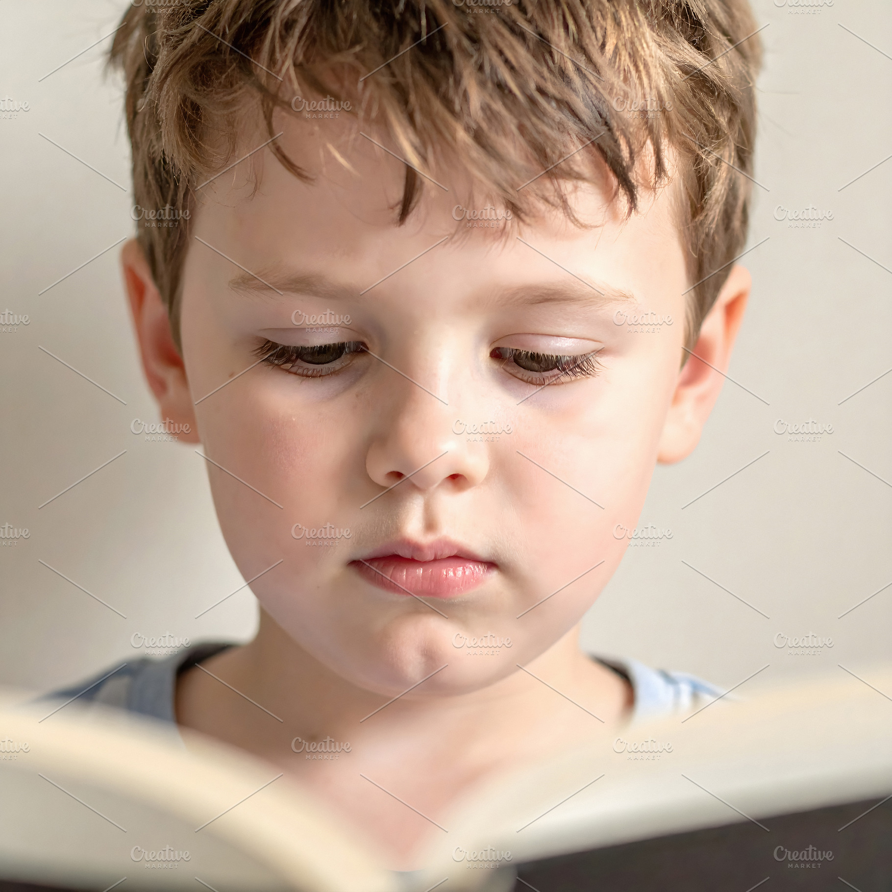 Young boy reading attentively holding open book pages, a Person Photo by GoodGoods