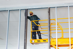 Construction worker installing drywall on a mobile elevating work platform, an Industrial Photo by Antonio Gravante Market