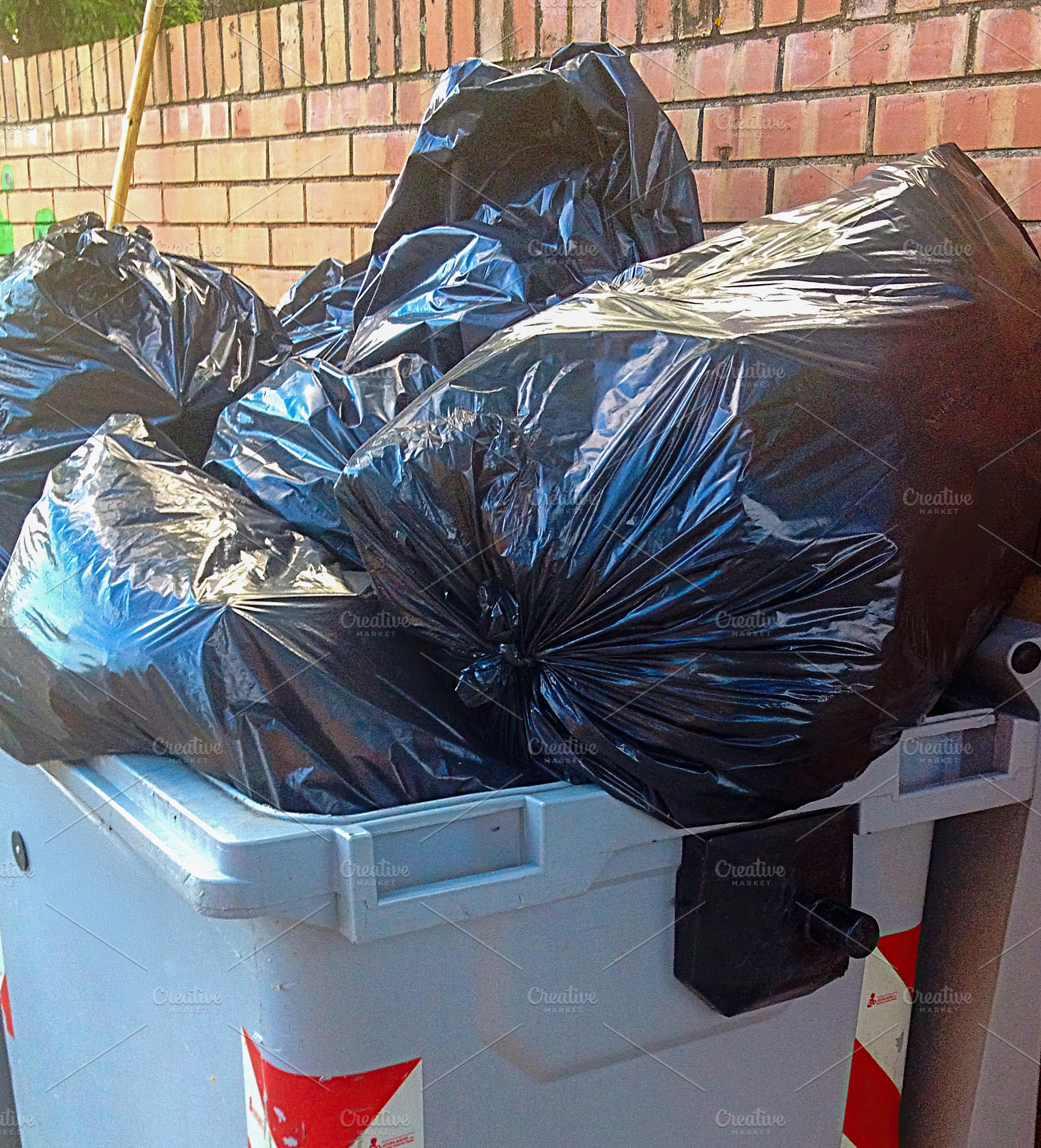 Overflowing dumpster with black garbage bags near brick wall, an Industrial Photo by Antonio Gravante Market