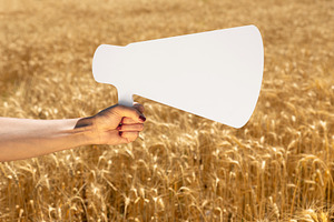 Female hand holding a white megaphone cutout over a ripe wheat f, a Business Photo by Ales Munt