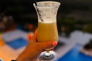 Tropical cocktail held against a sunset near a pool in a serene resort. Algarve, a Photo by AS photostudio