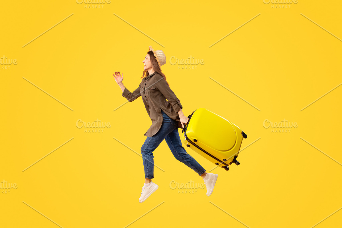 Female Tourist Running In Mid Air Carrying Suitcase, Yellow Background, a Photo by Prostock-Studio (Photo 1 of 2)