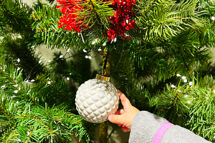 Child decorating Christmas tree with ornaments and lights, a Photo by AS photostudio