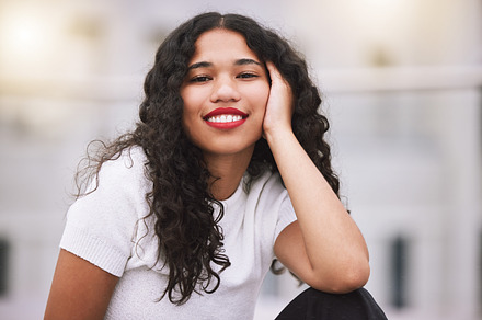 Beautiful mixed race fashion woman sitting outside in the city during the day. Young hispanic woman looking stylish and trendy, smiling and happy while outdoors in summer. Carefree and fashionable, a Photo by Peopleimages.com