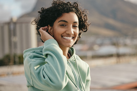 Face, smile and happy young woman feeling free and happy while smiling outside against an urban city background. Portrait of a indian female with an attractive, trendy or edgy style while on rooftop, a Photo by Peopleimages.com