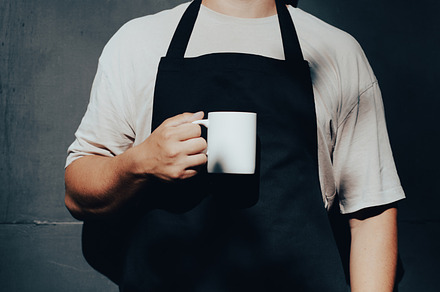 Man in apron holding white cup mockup against dark background. Barista with cup, a Person Photo by photoguns