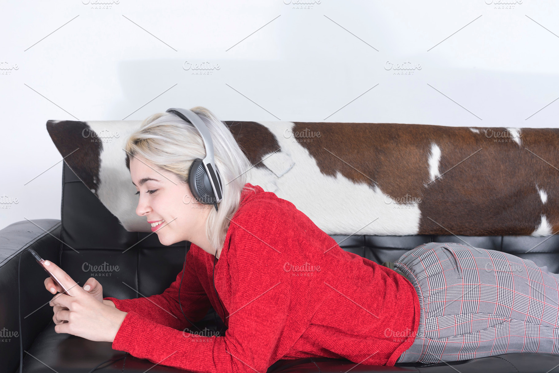 Blonde woman using mobile and listening music by headphones while lying on leat, a Person Photo by 2Design