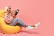 Joyful woman playing video games with joystick, sitting on beanbag chair over p, a Photo by Prostock-Studio (Thumbnail 1 of 2)