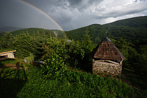 Rustic hut and rainbow in lush green countryside under moody sky, a Photo by AS photostudio