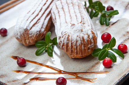 Cream eclairs choux pastries served with fresh cranberries on a