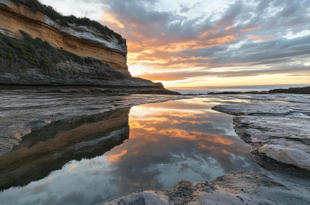 Sunset over rocky coastline with ref, a Photo by Tanuart