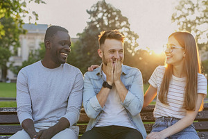Three friends laughing together on park bench, a Photo by DanFLCreativo