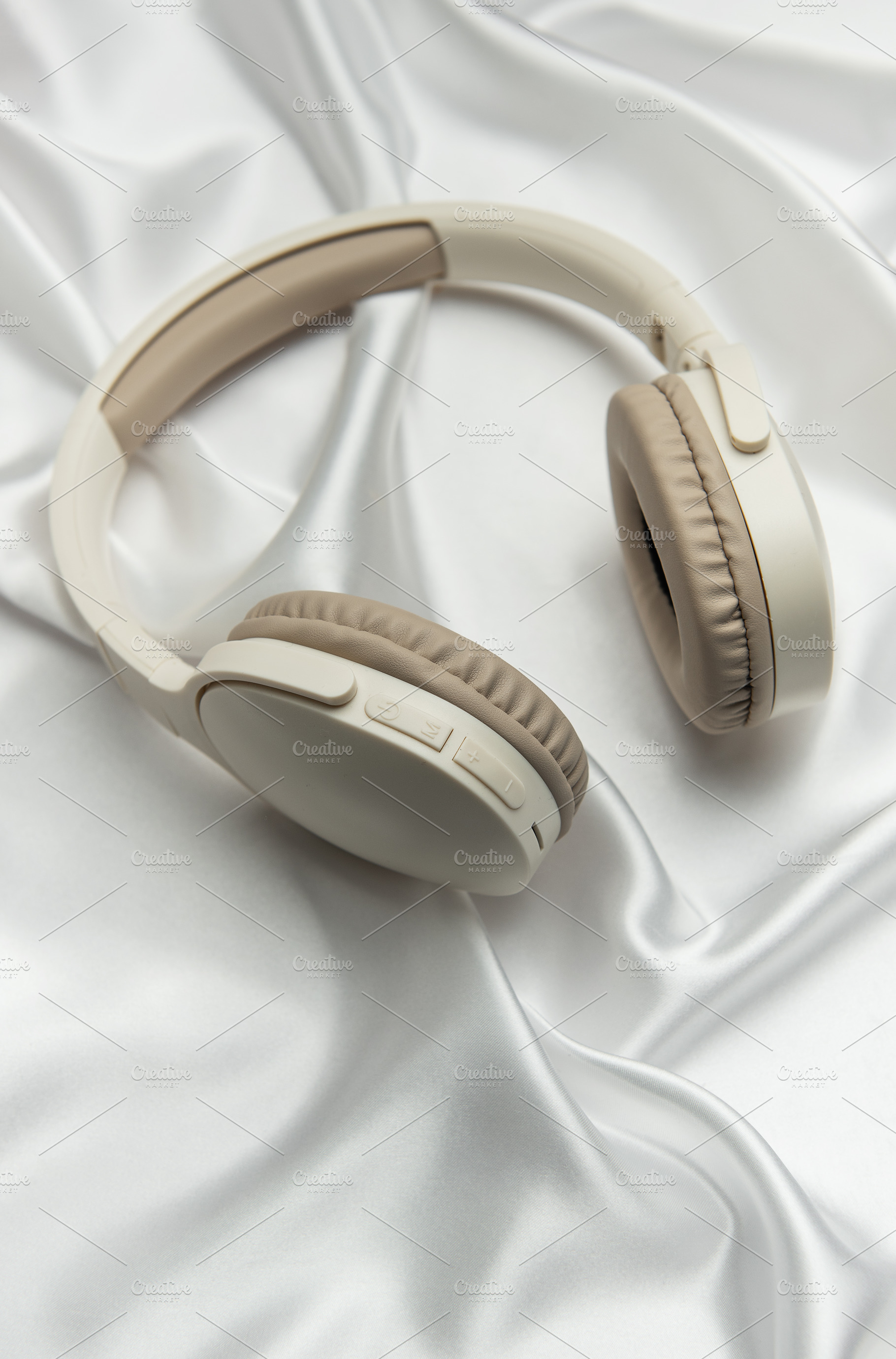 Modern wireless headphones lying on white silk background, a Technology Photo by Olena Rudo