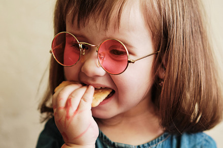 Portrait of a small girl in pink glasses. Cute infant girl eats a cookie., a Person Photo by Rohan Photography