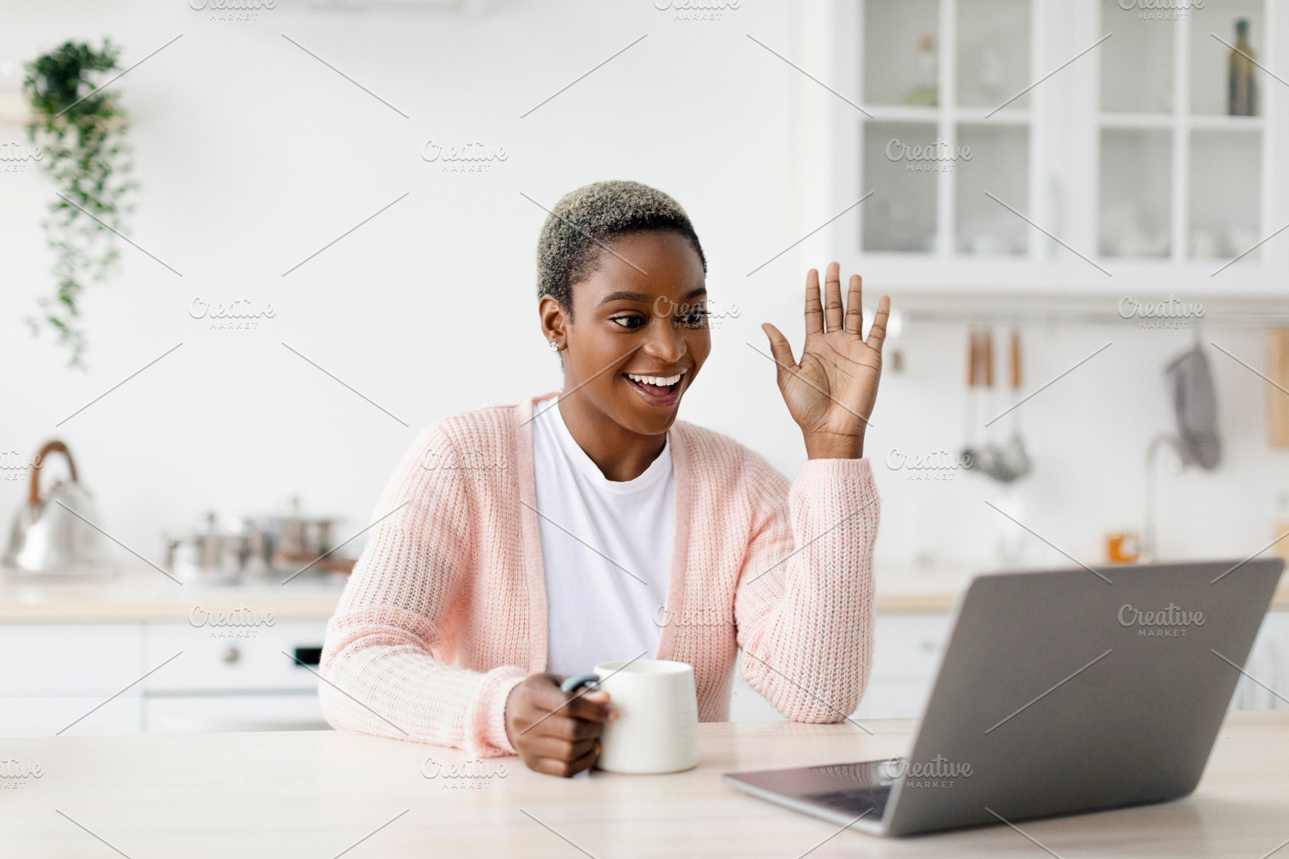 Cheerful young pretty black woman with cup of favorite drink, waves hand to lap, a Person Photo by Prostock-Studio