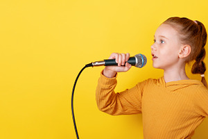 Confident young girl in yellow sweater singing with microphone a, a Person Photo by Ales Munt