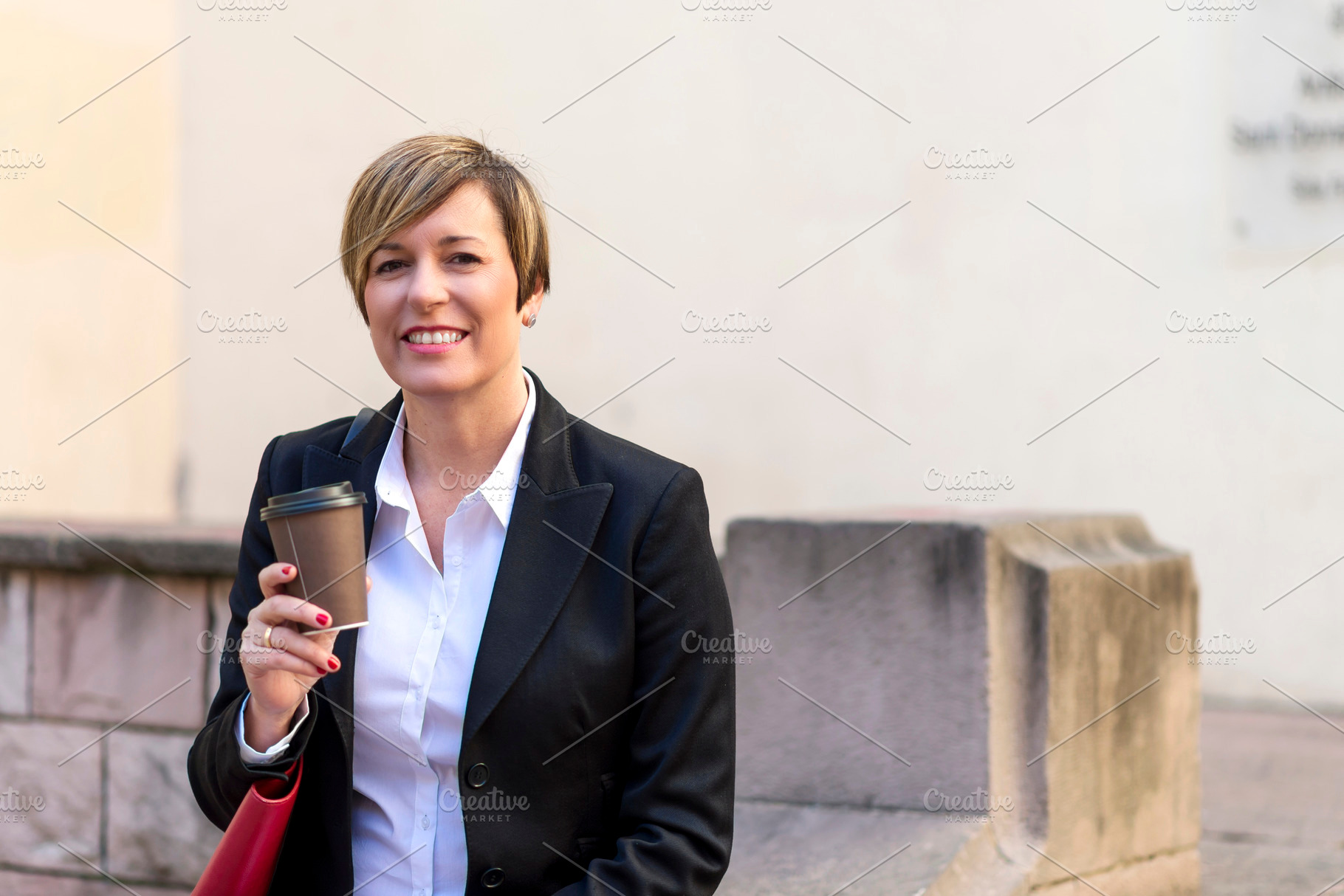 Businesswoman holding coffee in urban setting, a Photo by RF Images