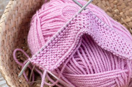 Piece of knitting with needles and pink yarn skein in wicker basket, on wooden, an Arts & Entertainment Photo by iuliia_n