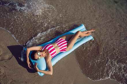 sexy woman in a striped swimsuit and sunglasses lies on blue air mattress on th, a Person Photo by SaulichPhoto