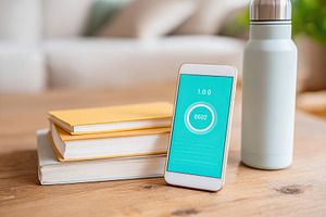 Smartphone and water bottle on wooden desk with books during study session, a Photo by AlyaAnd