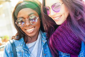 Two smiling young women wearing sunglasses are posing together outdoors, a Person Photo by Antonio Gravante Market
