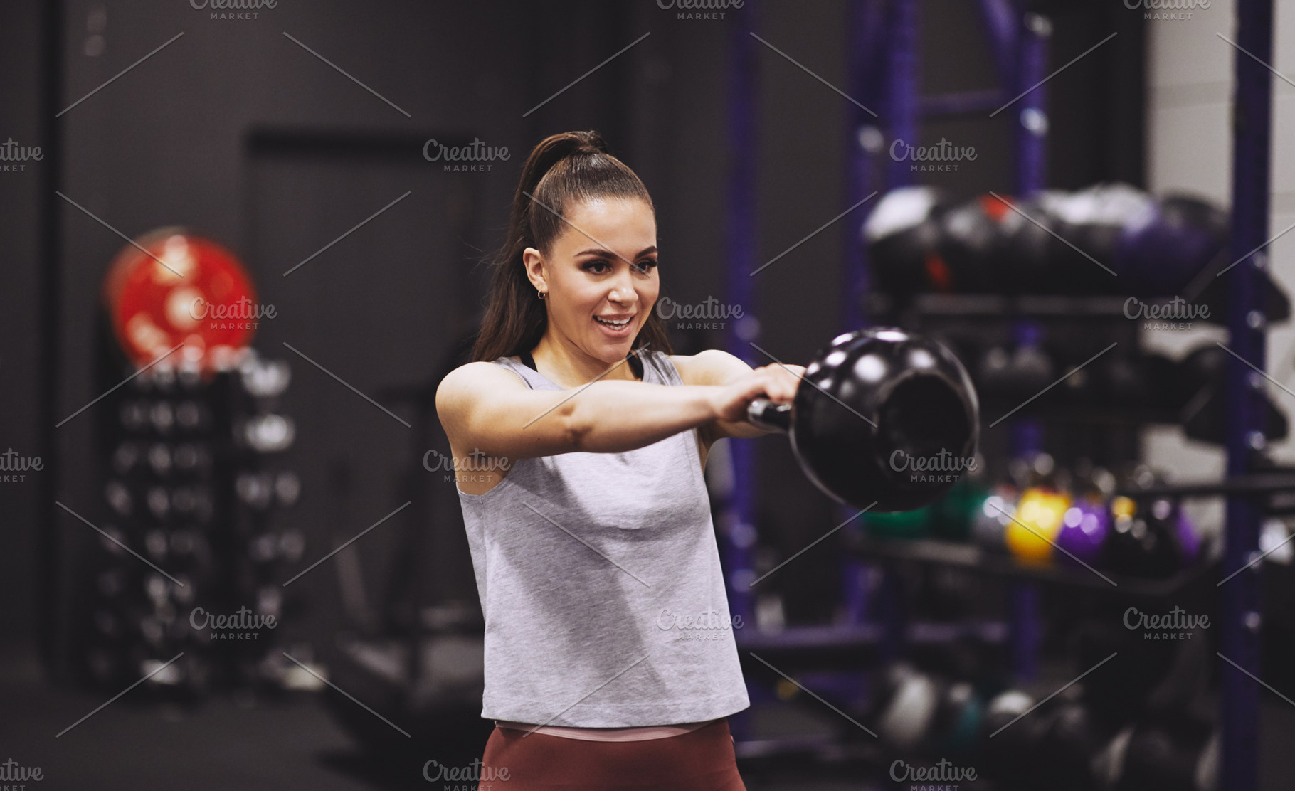 Smiling young woman swinging a dumbbell at the gym, a Sports & Recreation Photo by Stefan & Janni