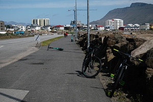 Bicycles and scooters parked near a pathway in Akranes under mountain view, a Photo by AS photostudio