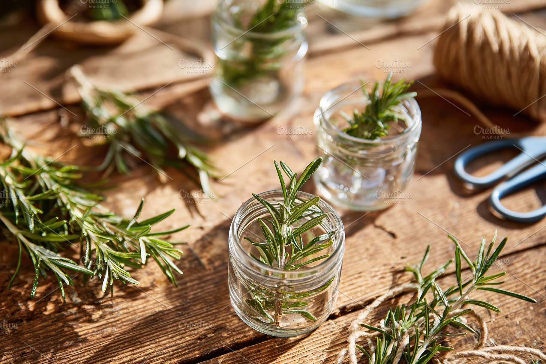 Fresh rosemary sprigs in glass jars on wooden table with twine and scissors, a Photo by AlyaAnd