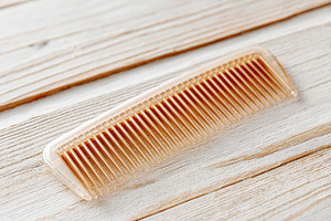 Fine-toothed plastic comb resting on a textured wooden surface in a bright sett, a Photo by AlyaAnd