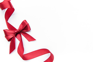 Red satin ribbon forming bow on white background, a Photo by Olena Rudo
