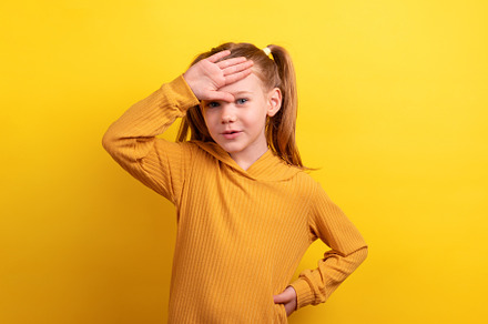 Young girl in mustard sweater with hand on her forehead, posing