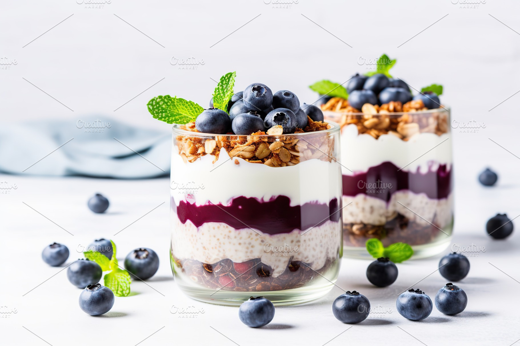 Chia pudding with blueberry and granola in glass on white background, a Food & Drink Photo by AlyaAnd