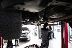 Mechanic working under lifted car at automotive repair garage during maintenanc, a Transportation Photo by AS photostudio