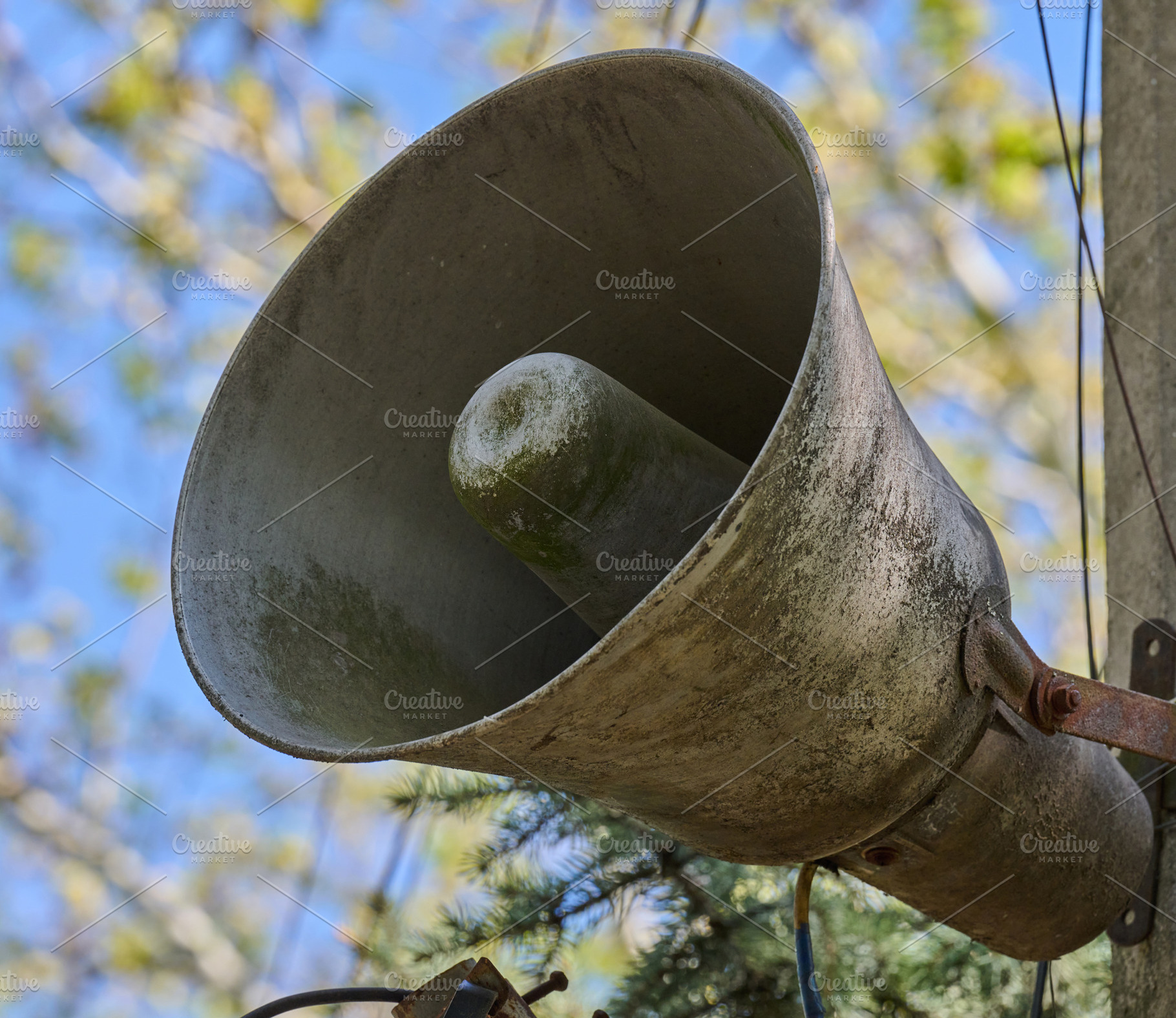 An old, dirty, grey loudspeaker is mounted on a pole. In the bac, an Abstract Photo by ndanko